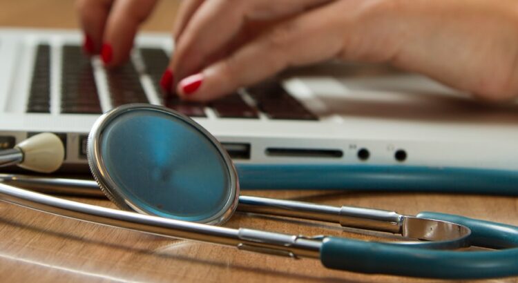 person sitting while using laptop computer and green stethoscope near